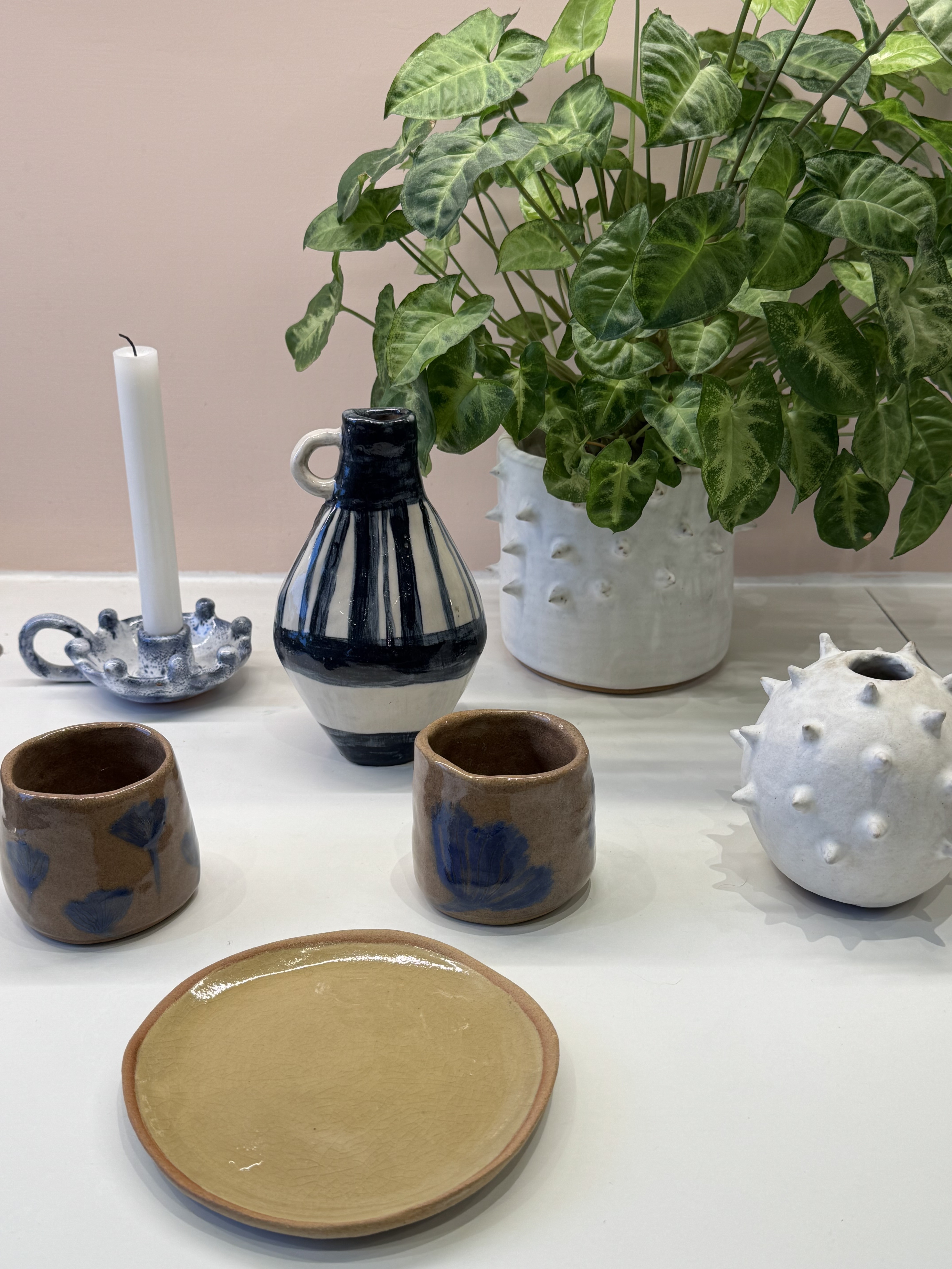 A tablescape of handmade ceramic pieces including a striped jug, spiked vases and a plate